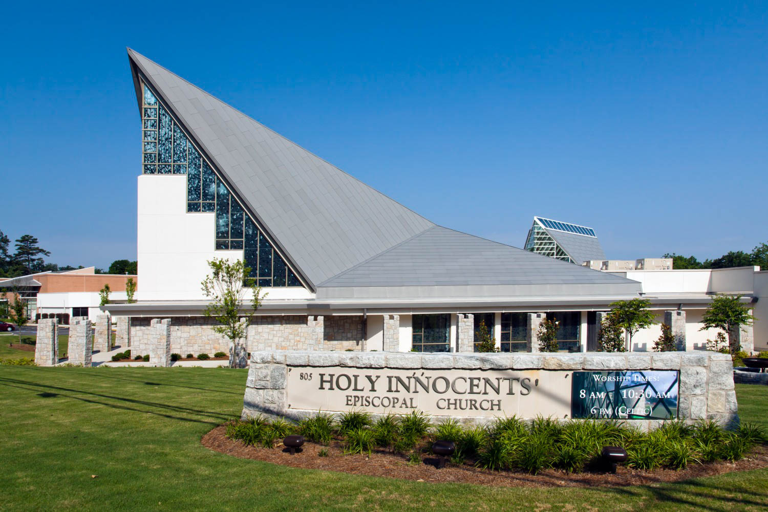 Modern church building with a steeply angled roof and large stained glass windows, with a sign reading “Holy Innocents’ Episcopal Church” in front.