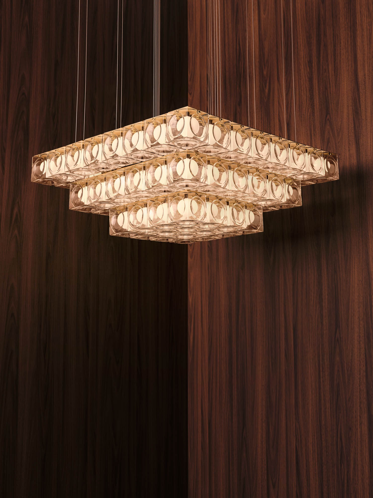 Square, tiered chandelier with multiple small round lights, suspended from the ceiling, set against dark wood-paneled walls.