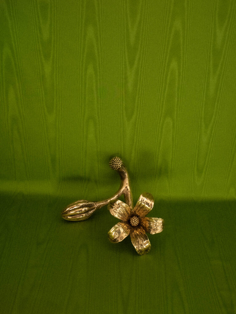 A metallic flower ornament with stem, bud, and petals rests on a textured green surface and background.