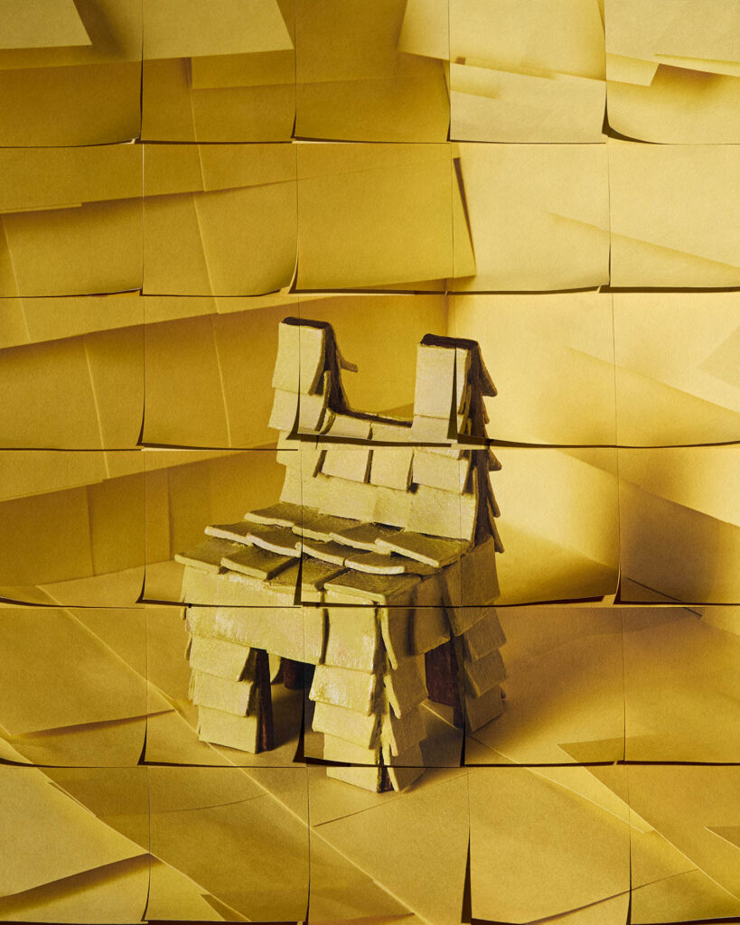 A small chair made of layered yellow sticky notes sits in front of a wall also covered in yellow sticky notes.
