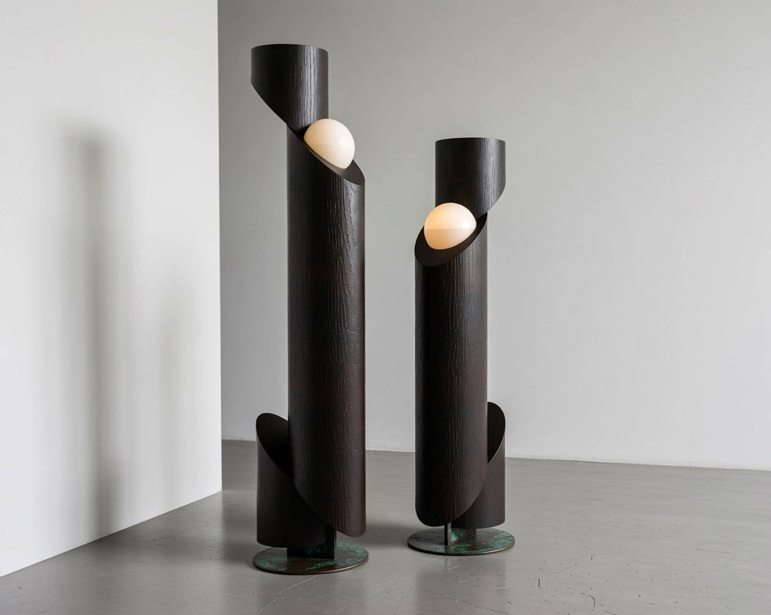 Two modern floor lamps made of dark, cylindrical wood with white spherical bulbs partially enclosed by asymmetrical cutouts, standing on circular bases in a minimal room.