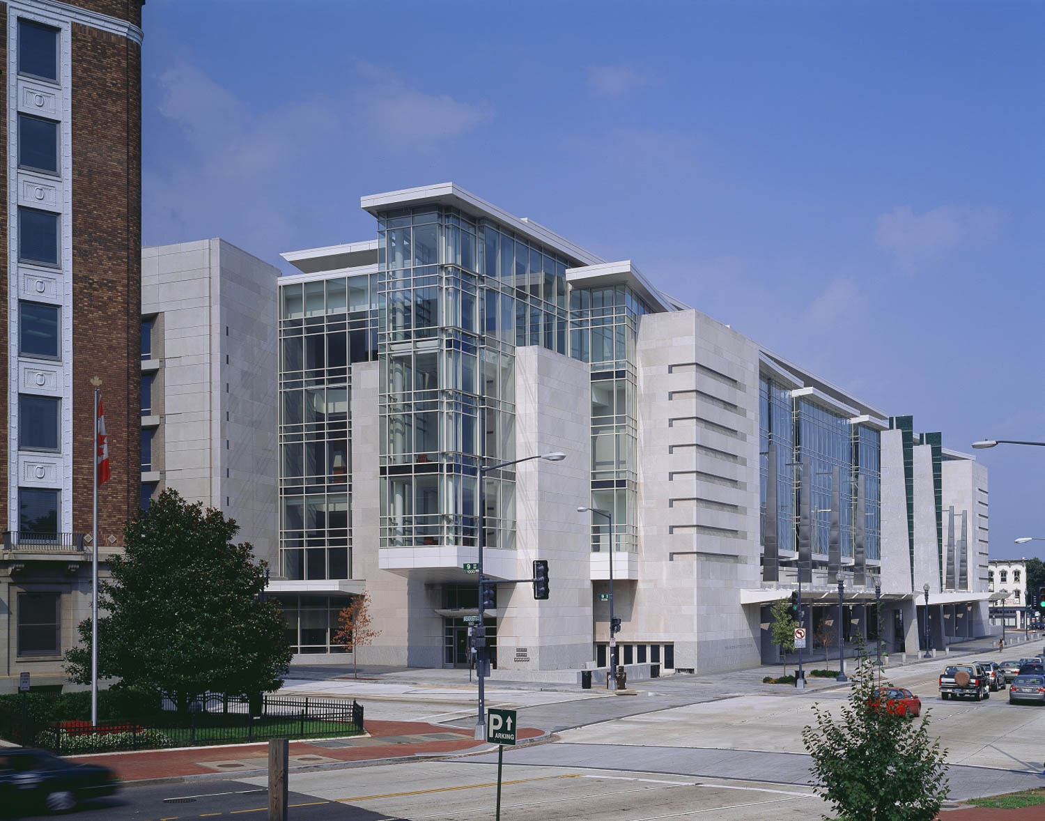 A modern convention center with large glass windows and white facade stands along a city street with sparse traffic and trees.