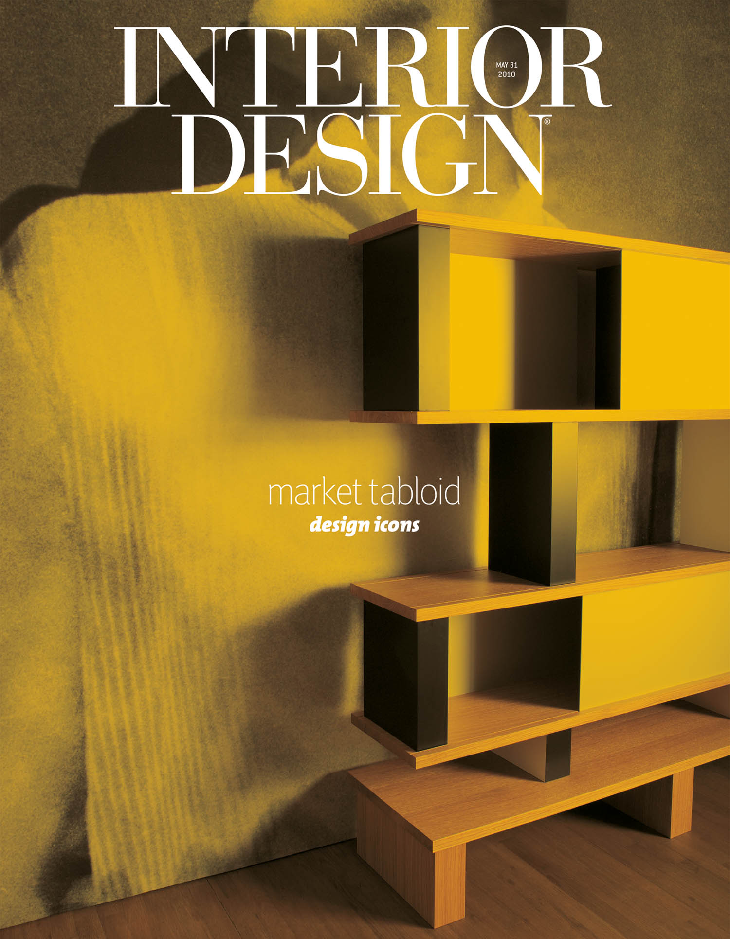 A modern yellow and black shelving unit stands against a textured wall in a minimalist room. The magazine cover reads “Interior Design” and “market tabloid design icons.”.