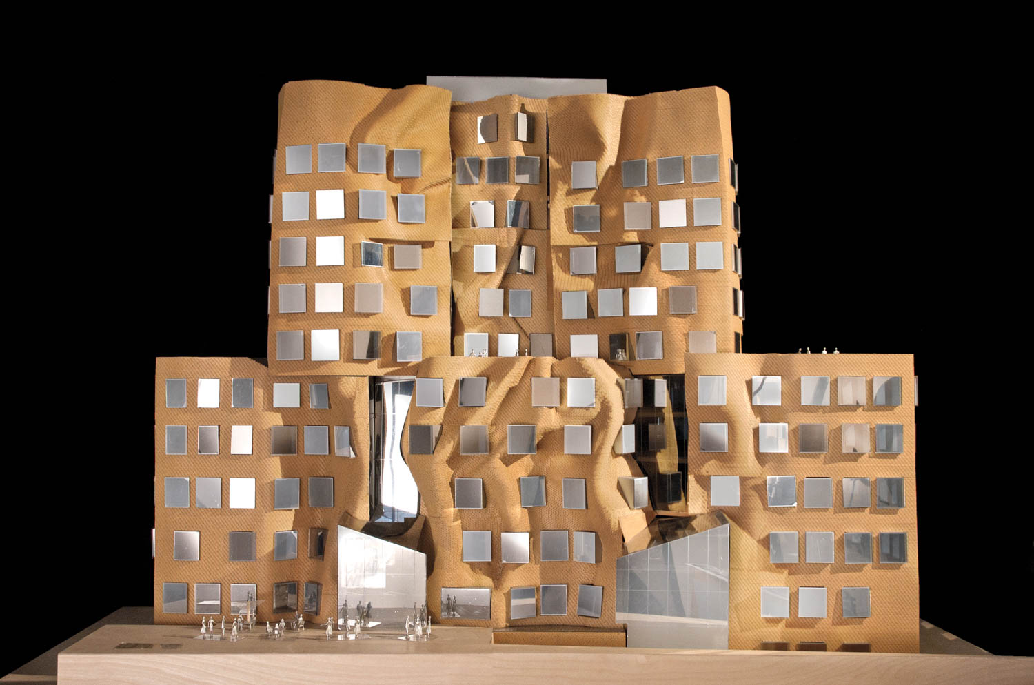 Architectural model of a building with irregular, curved surfaces and square windows, featuring a gold-colored exterior on a wooden base against a black background.
