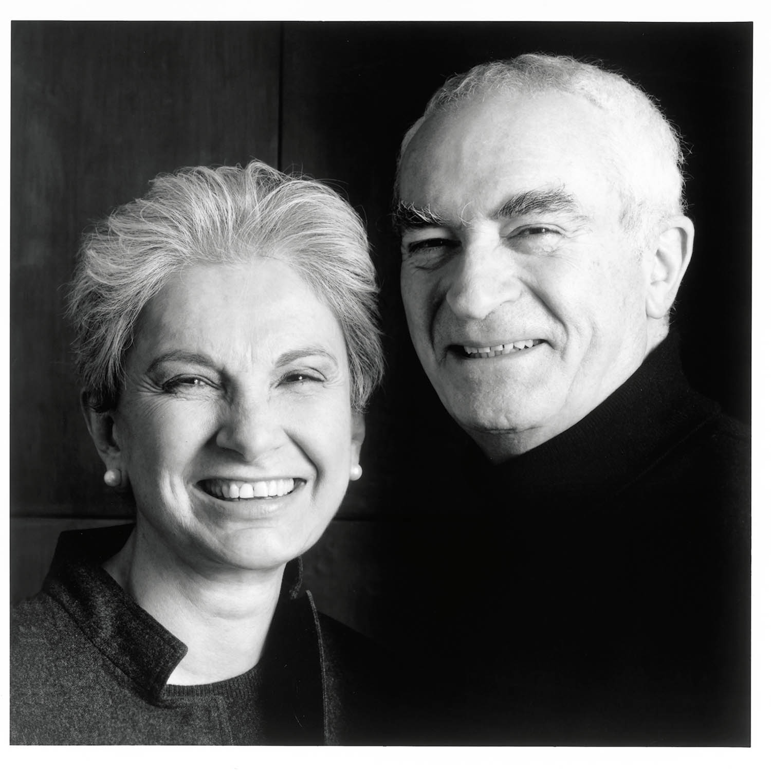 Black and white portrait of an older woman and man standing close together, both smiling, with the woman in front and the man slightly behind her.