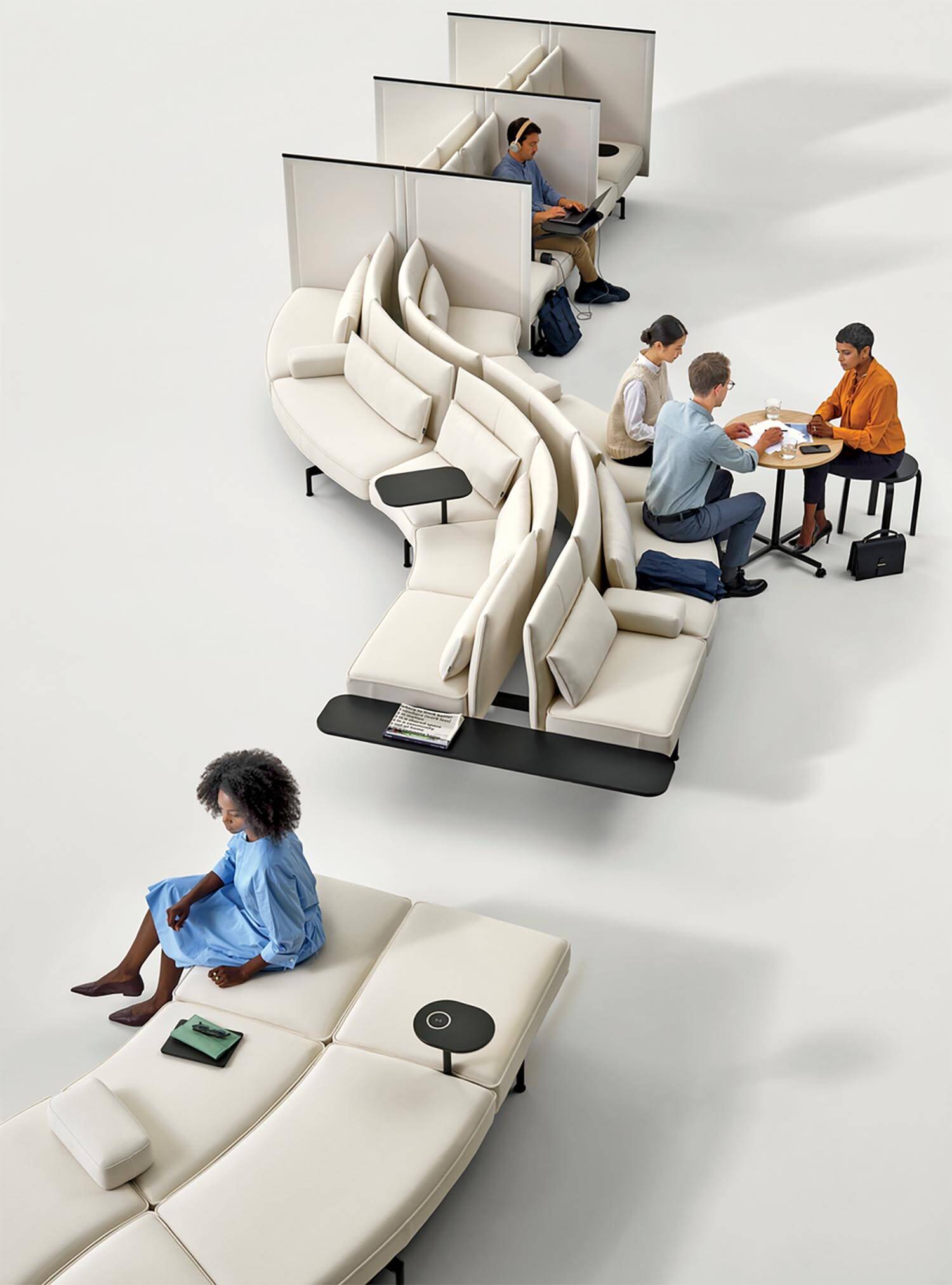 Office lounge with modular white seating; people are working, meeting, and relaxing, some using laptops and notebooks. The space includes desks, privacy panels, and small tables.