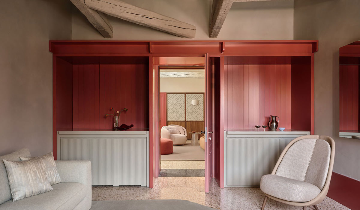 Modern living space with muted beige furniture, red accent walls, exposed beams, and an open doorway leading to another room with more seating—a refined interior reminiscent of the effortless style found at Elizabeth Unique Venice.