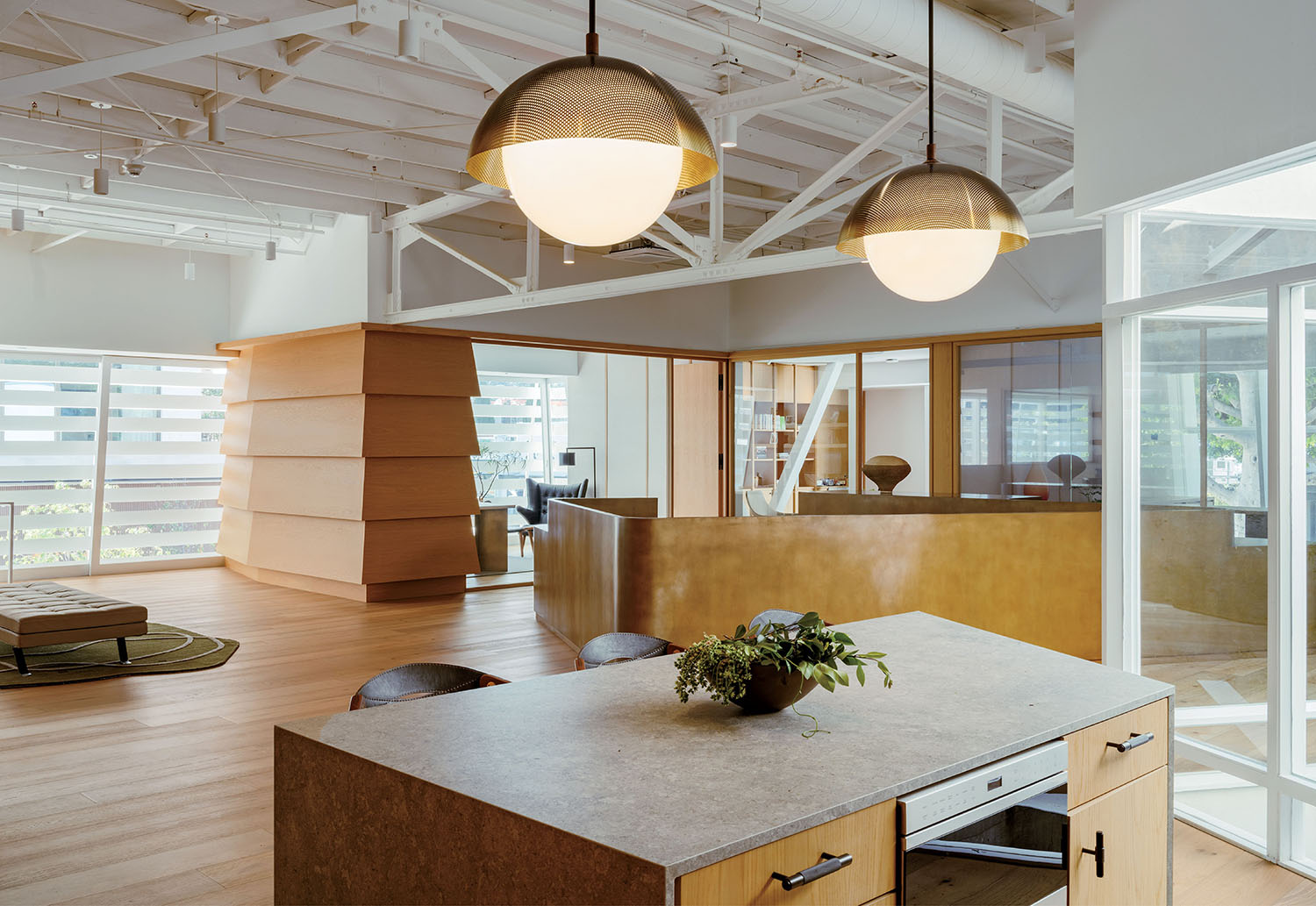 Modern office with wood accents, large pendant lights, glass walls, and indoor plants. Natural light enters through horizontal blinds and large windows.