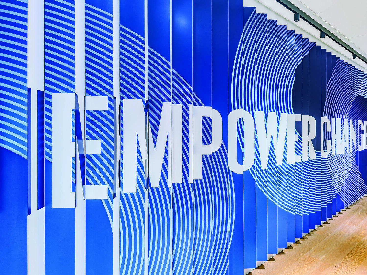 A blue wall with white concentric circle patterns and large bold white text that reads “EMPOWER CHANGE.”.