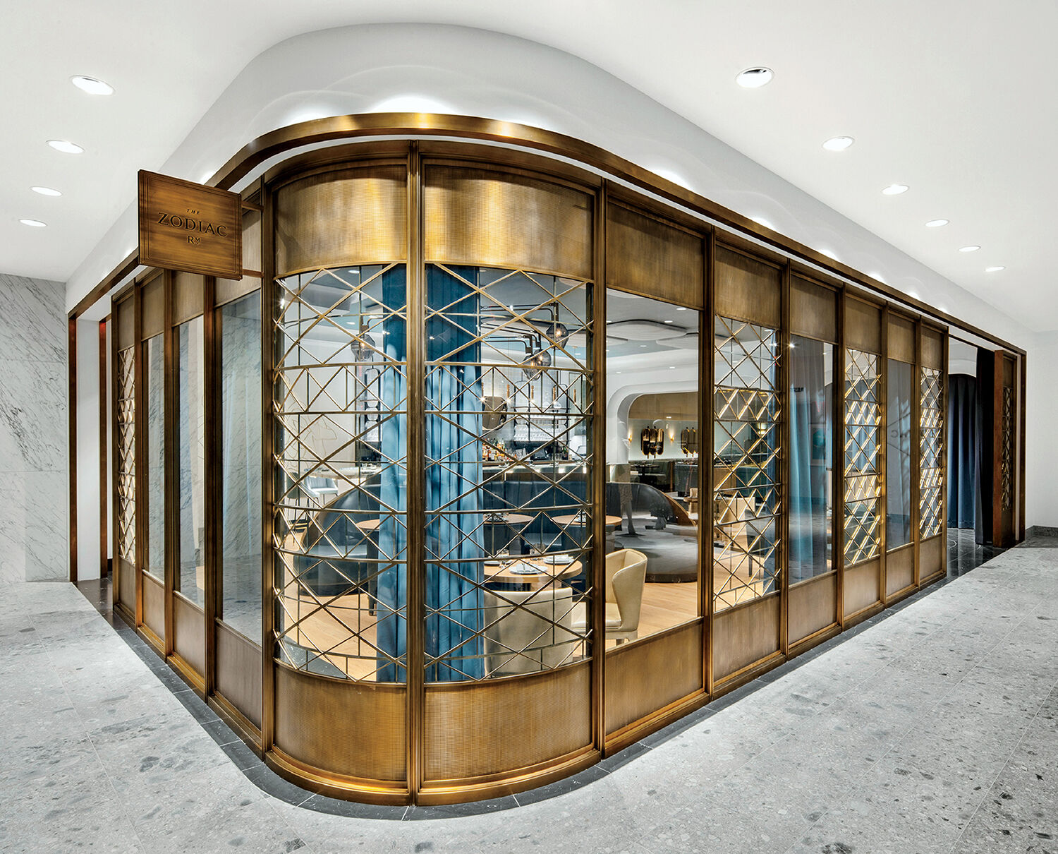 A store with curved glass walls and gold metal framing, featuring lattice-style panels and a modern interior with blue accents and seating.