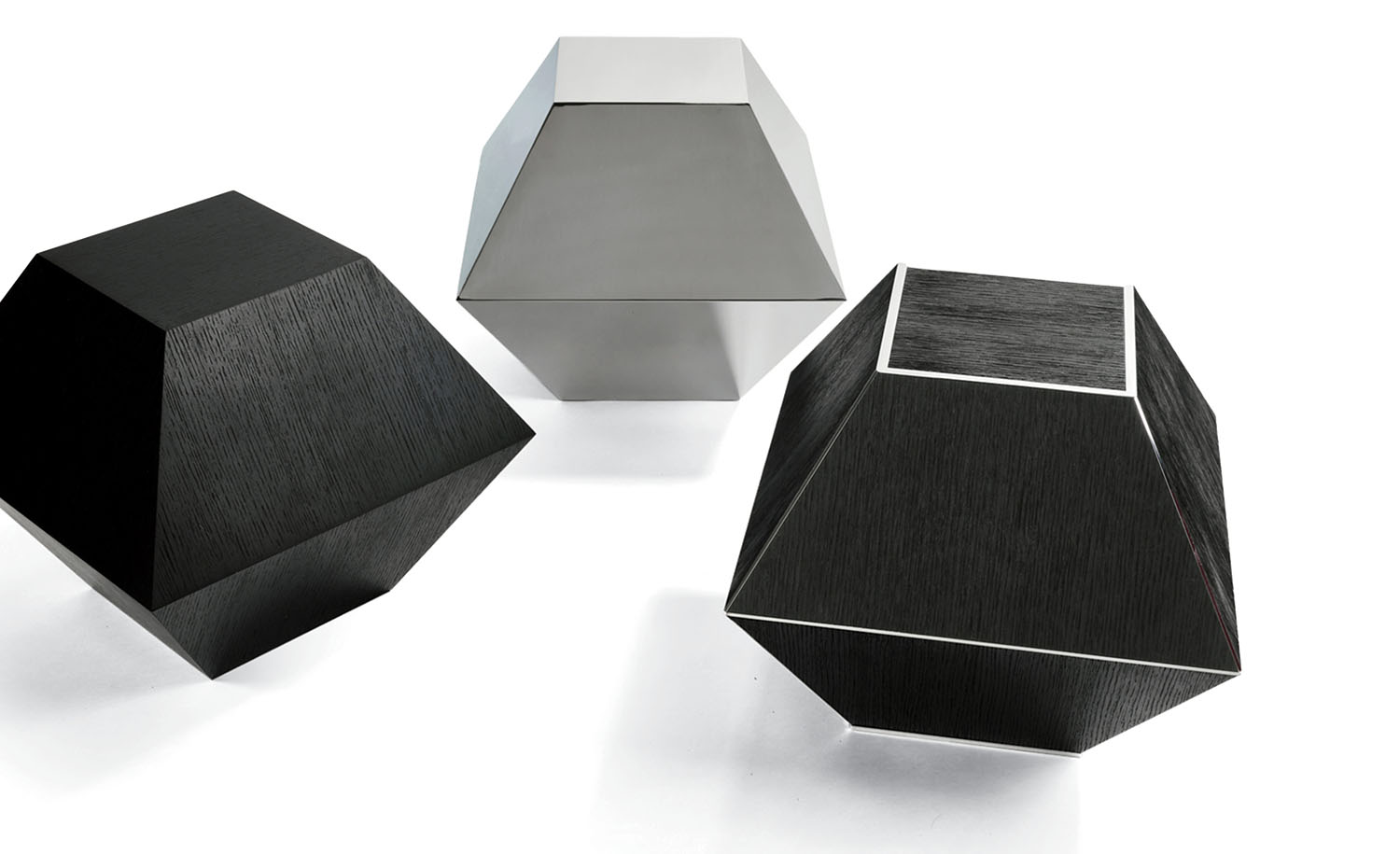 Three geometric, hexagonal prism-shaped objects, two black with white edges and one metallic, are arranged on a white background.