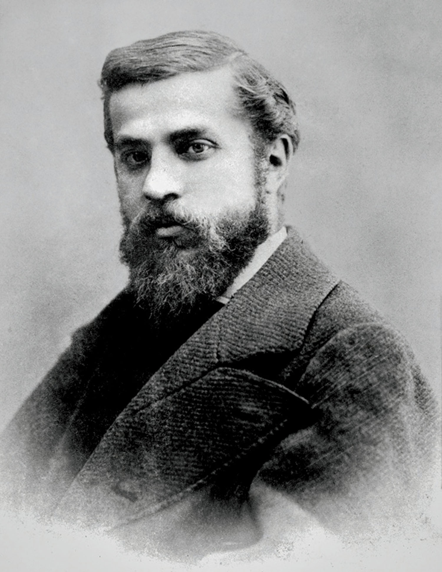 Black and white portrait of a bearded man in a suit, facing slightly to the side, looking directly at the camera with a neutral expression.
