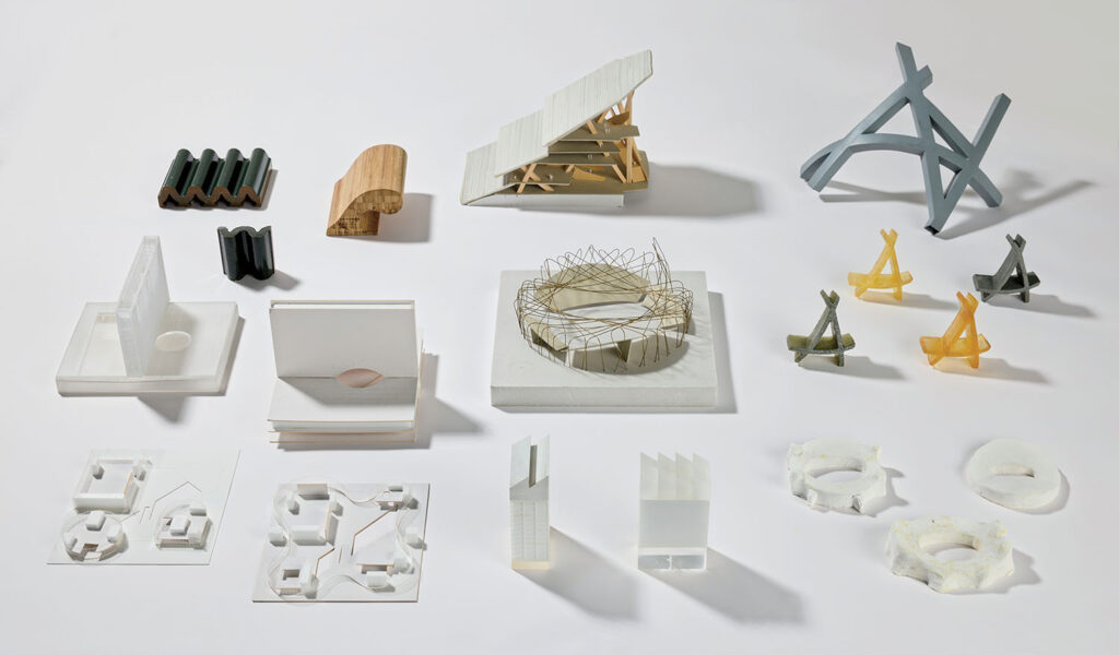 A collection of abstract architectural models made from various materials, arranged in four rows on a white surface.