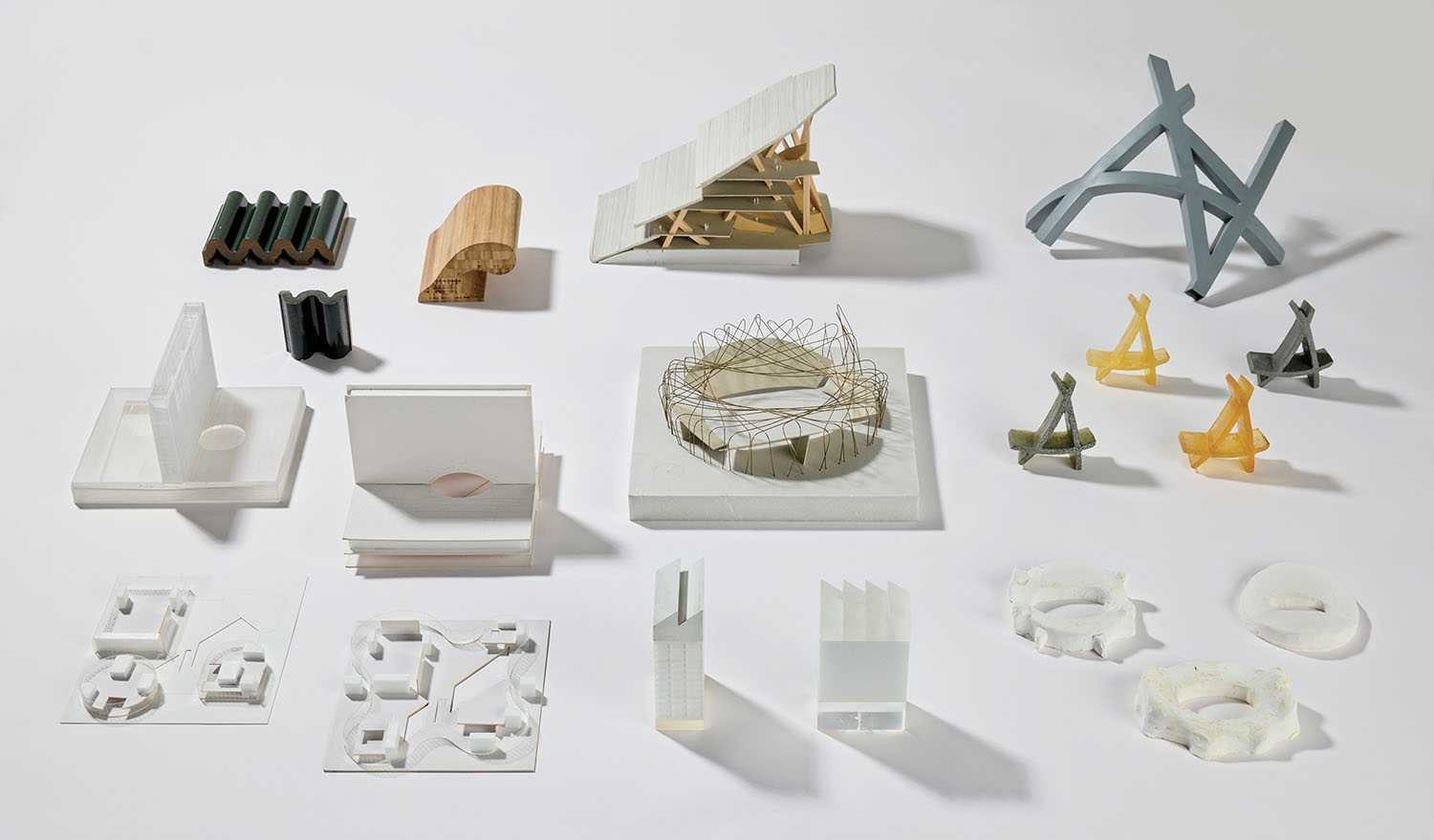 A collection of abstract architectural models made from various materials, arranged in four rows on a white surface.