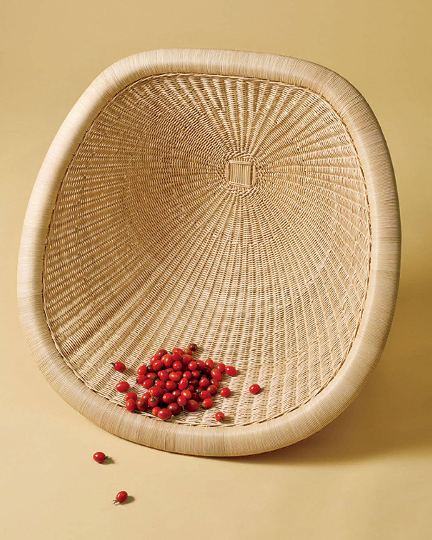 A woven wicker basket tipped on its side with a small pile of red berries scattered inside on a beige background.