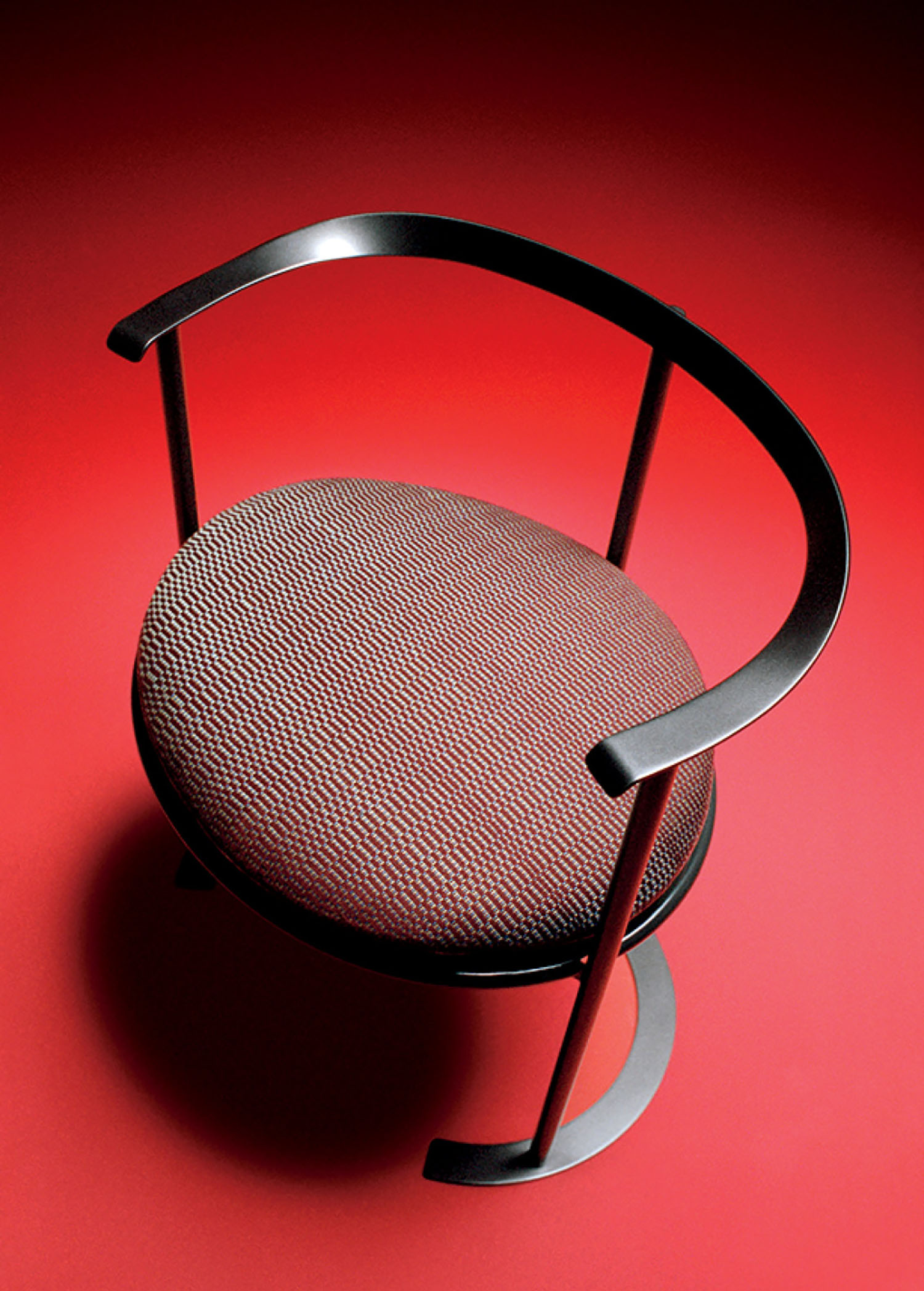 Modern chair with a round, textured fabric seat and black curved metal frame, photographed from above against a red background.
