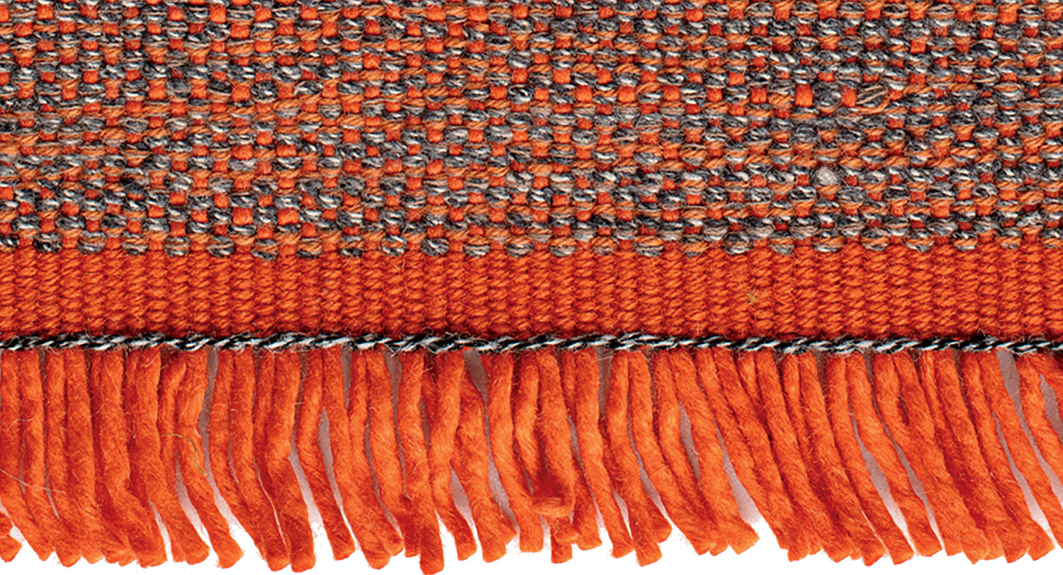 Close-up of a woven fabric with orange and gray threads, featuring a fringe of thick orange yarn hanging along the bottom edge.