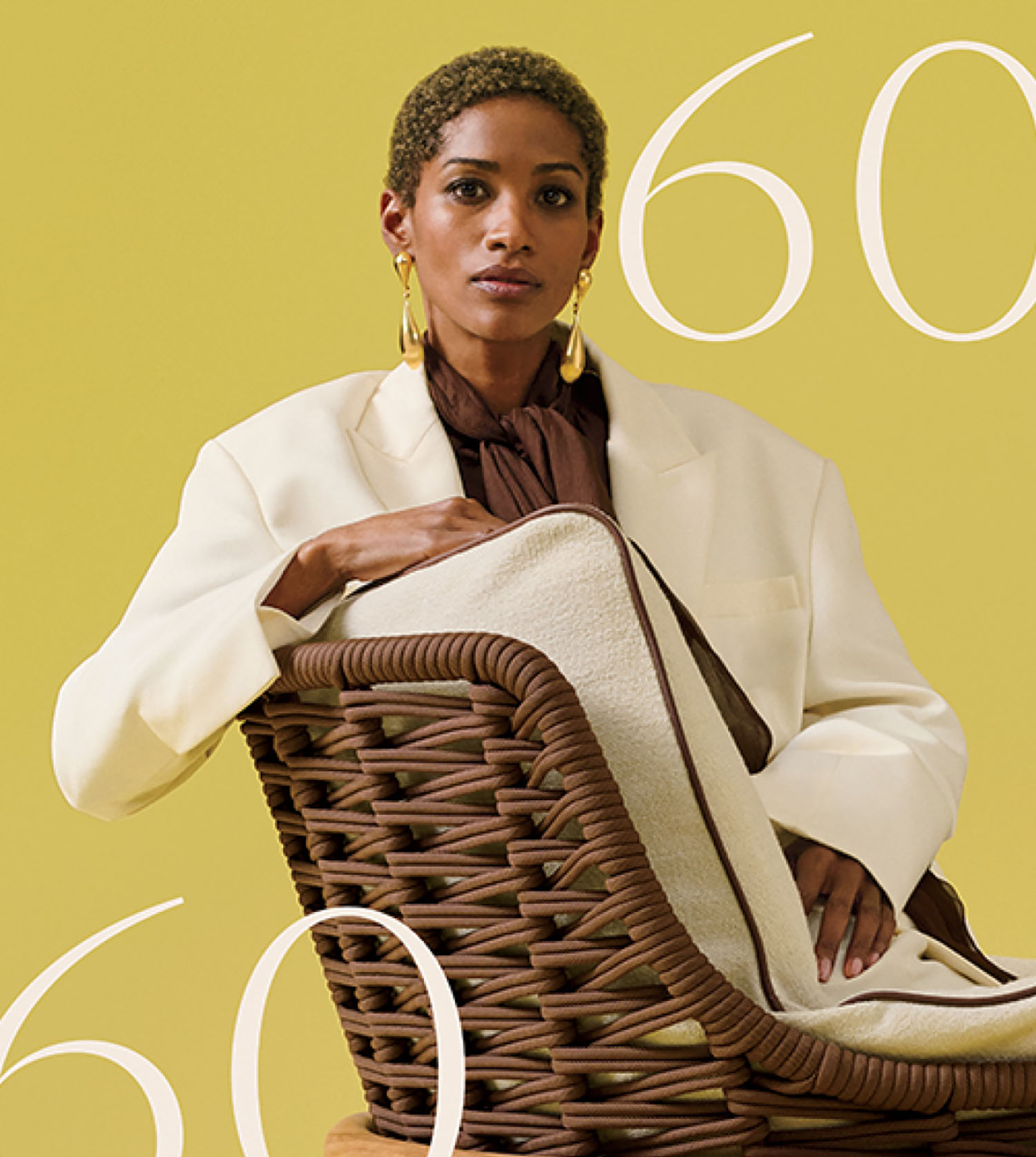 A person in a white blazer sits in a wicker chair against a yellow background with the number 60 partially visible in the image.