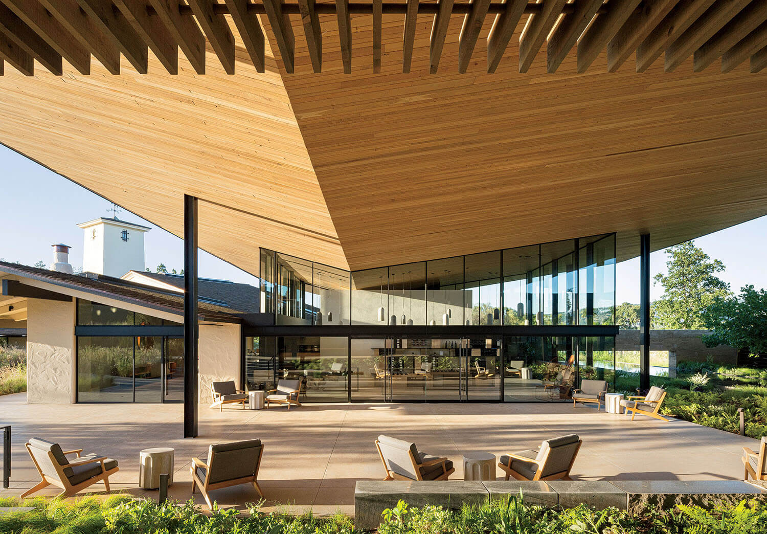 Modern covered patio with a large wood-slatted ceiling, glass walls, and outdoor lounge furniture.