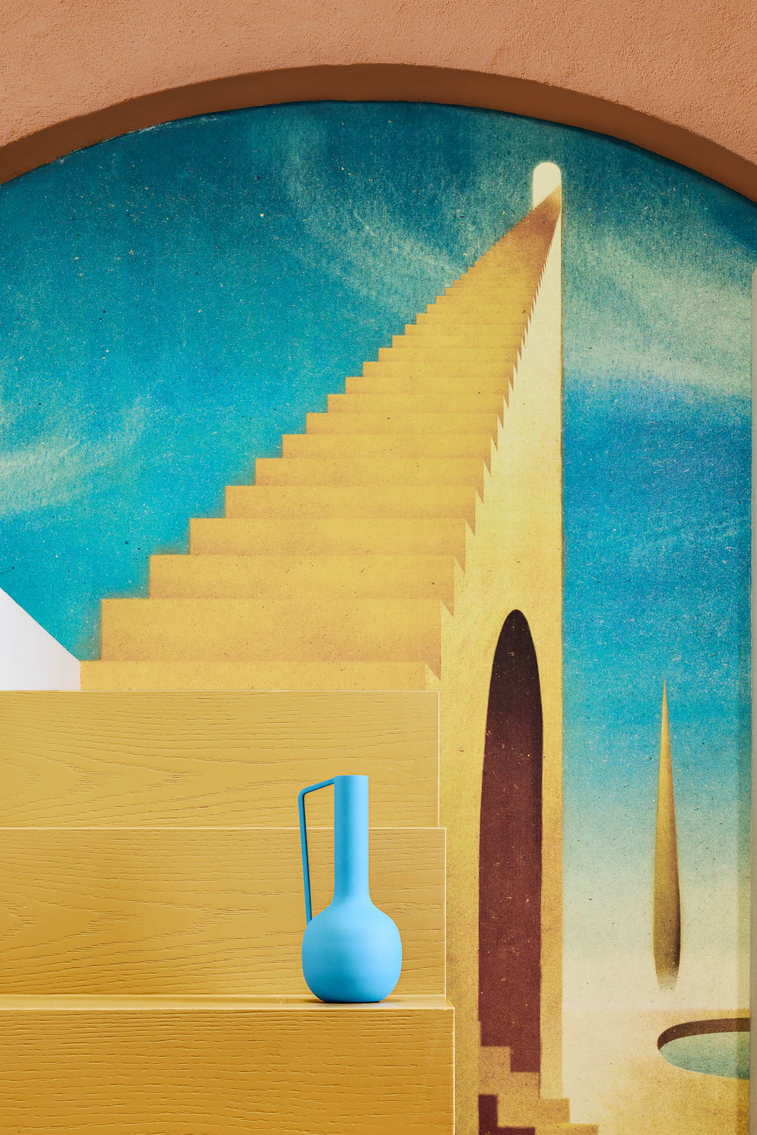 A blue ceramic jug sits on a yellow step in front of a mural depicting a staircase ascending into a blue sky.