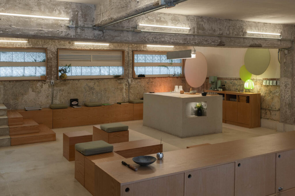 Minimalist cafe interior with wood seating, a central concrete counter, and textured concrete walls.