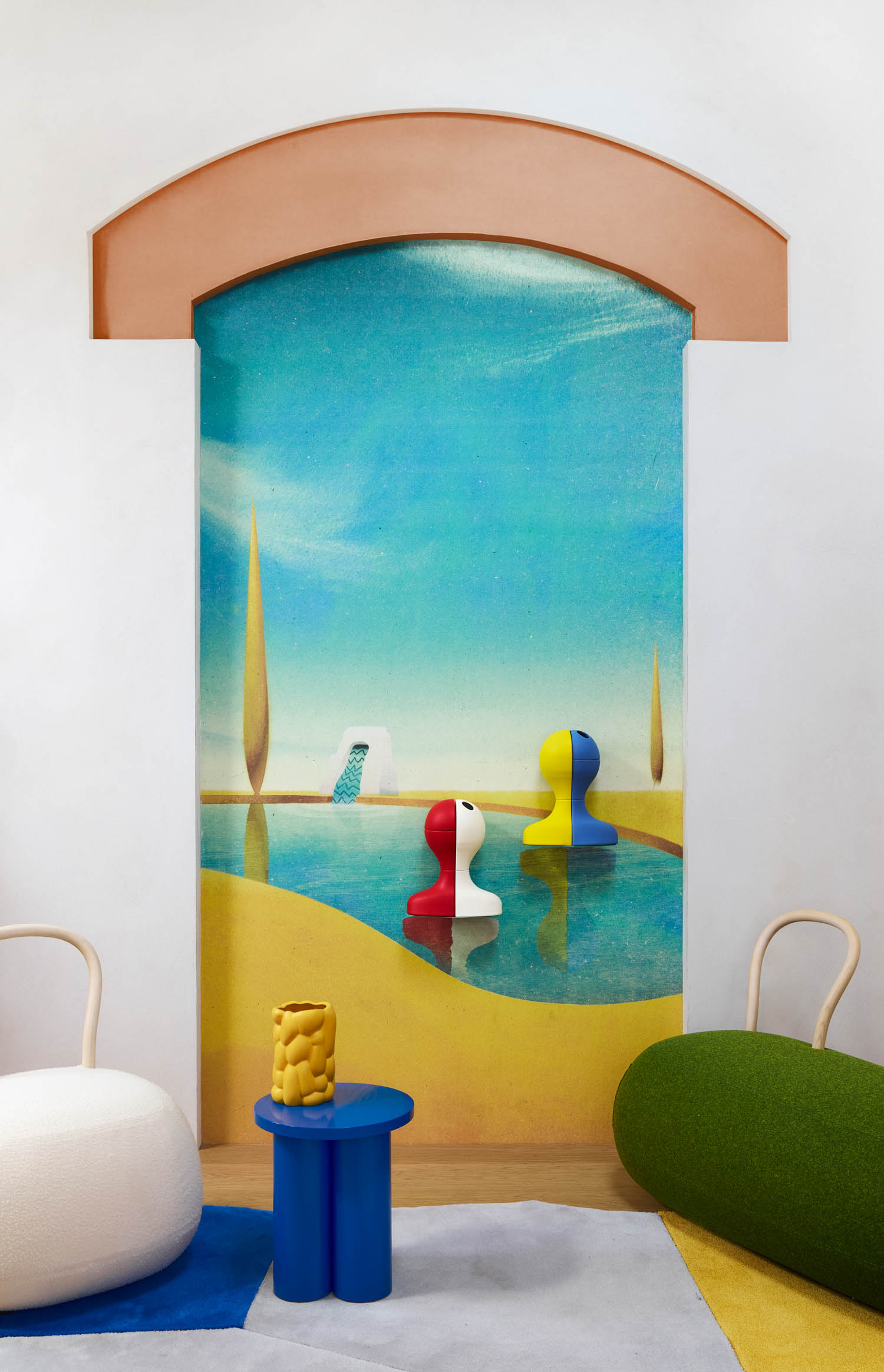 An arched wall mural of a surreal landscape with two abstract figures, positioned behind a small blue side table with a yellow textured vase, flanked by two rounded chairs.