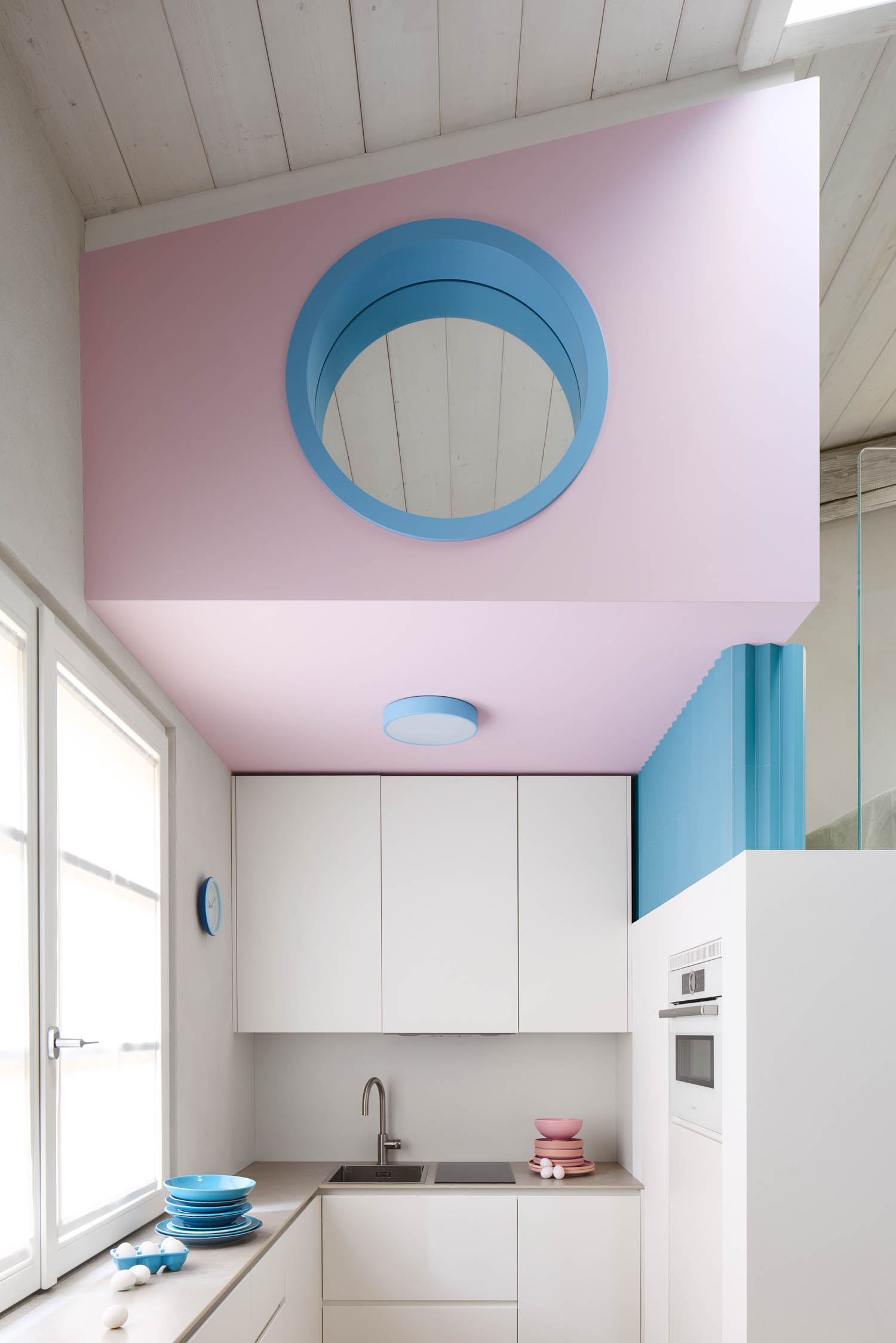 Small kitchen with white cabinets, a pink ceiling featuring a circular window, and blue accents.