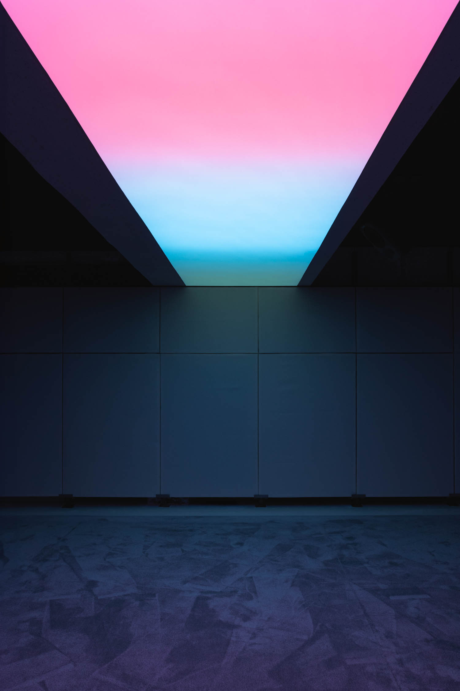 A rectangular ceiling panel glowing with a pink to blue gradient above a dark, paneled wall.