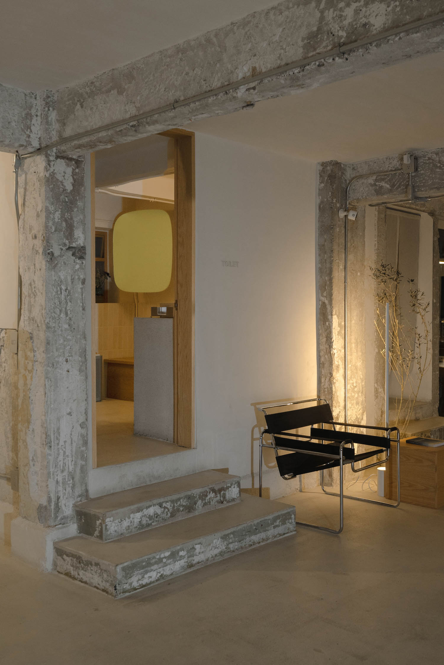 A black leather and metal lounge chair sits beside a concrete doorway leading to a room with a yellow wall accent.