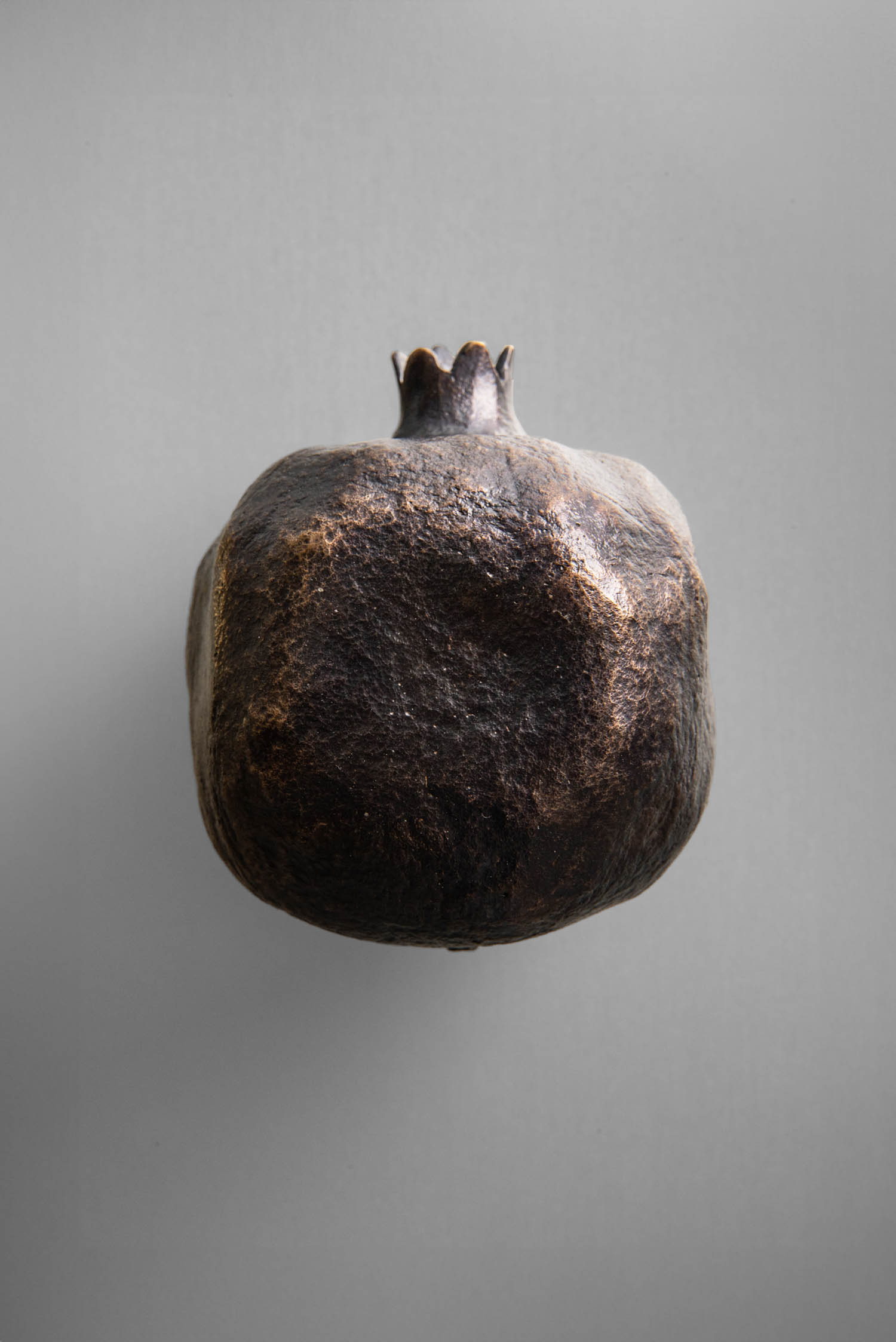 A dark, dried pomegranate centered on a plain gray background.