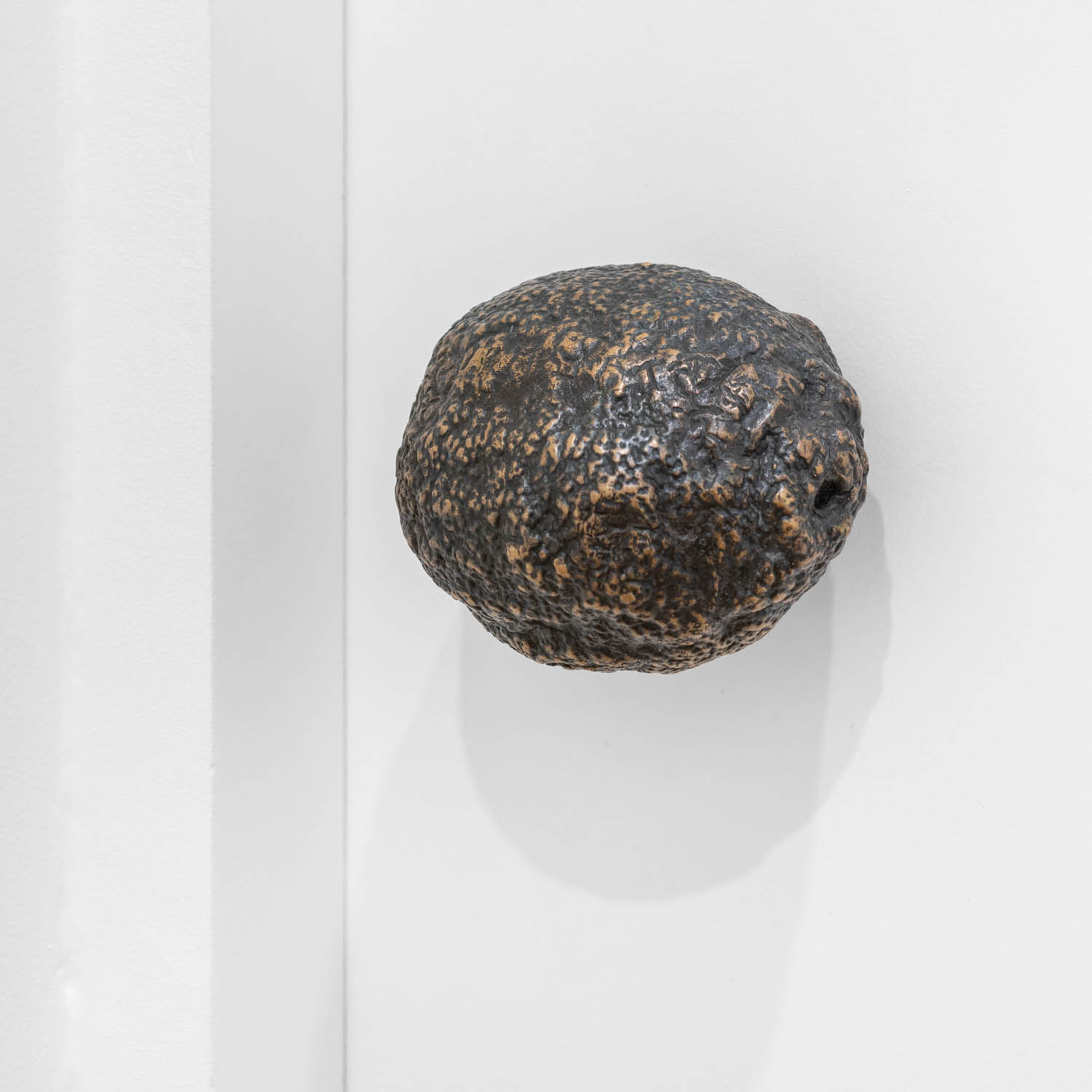 A dark, textured, spherical door knob attached to a white door.
