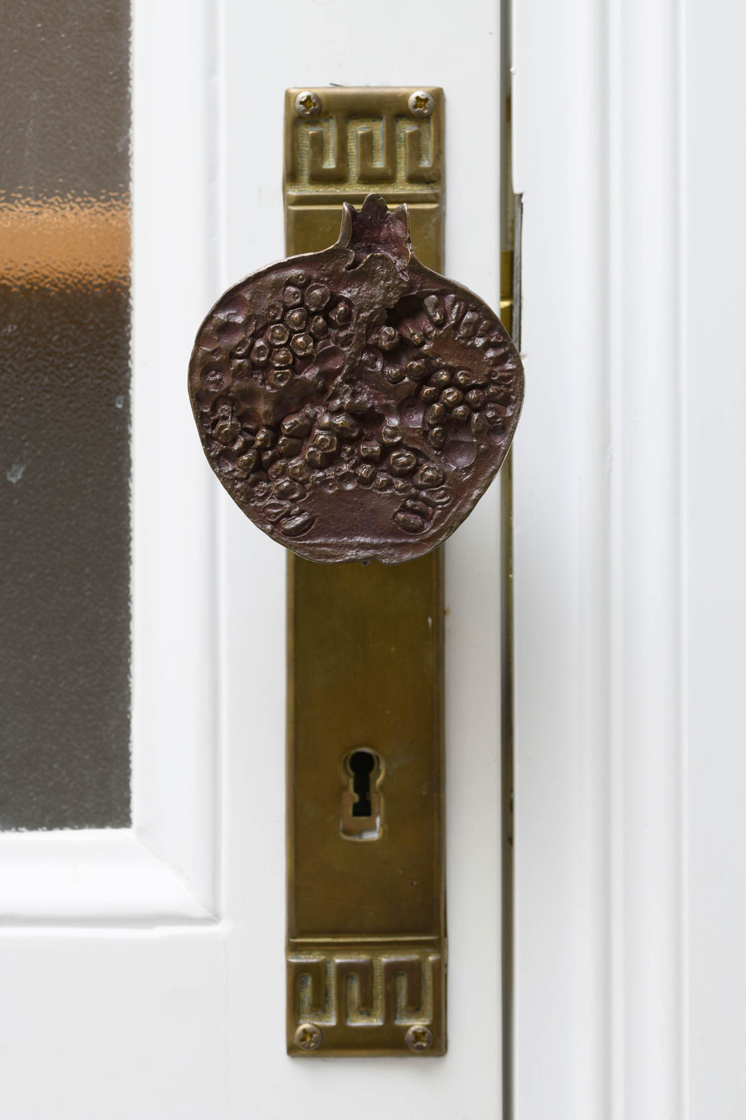 A brass door handle shaped like a pomegranate on a white door.