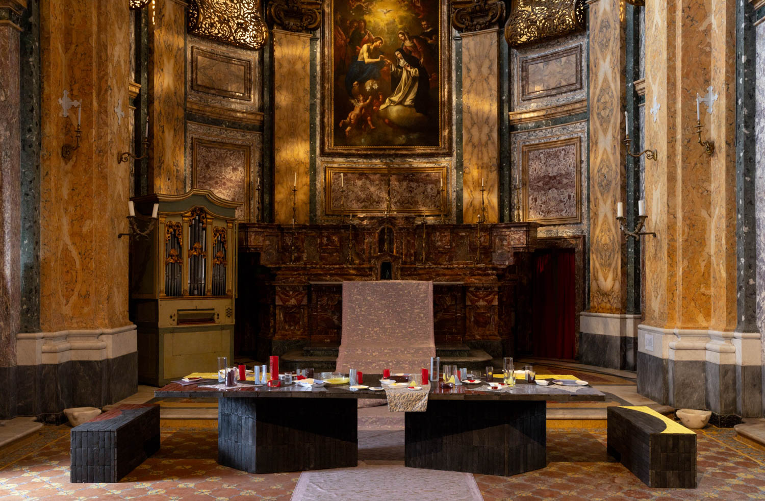 A long dining table set for a meal in the center of an ornate church interior.