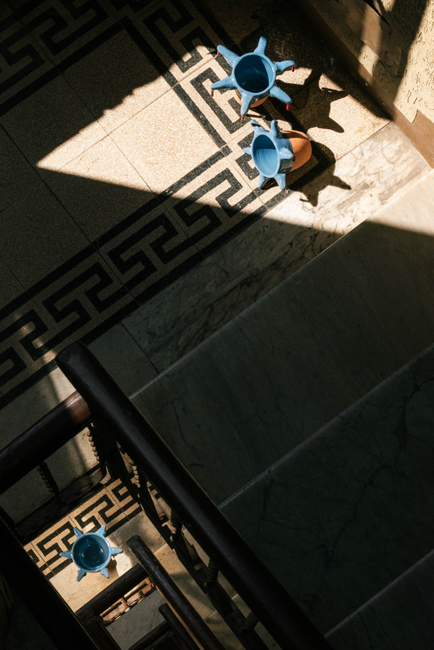 Three light blue ceramic planters on a tiled floor with a geometric pattern, seen from above near a wooden staircase.