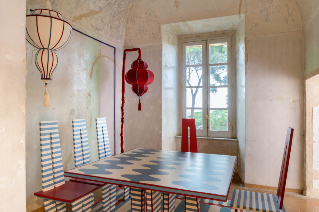A dining set with a patterned table and chairs, featuring two red lanterns in a rustic room with a window.