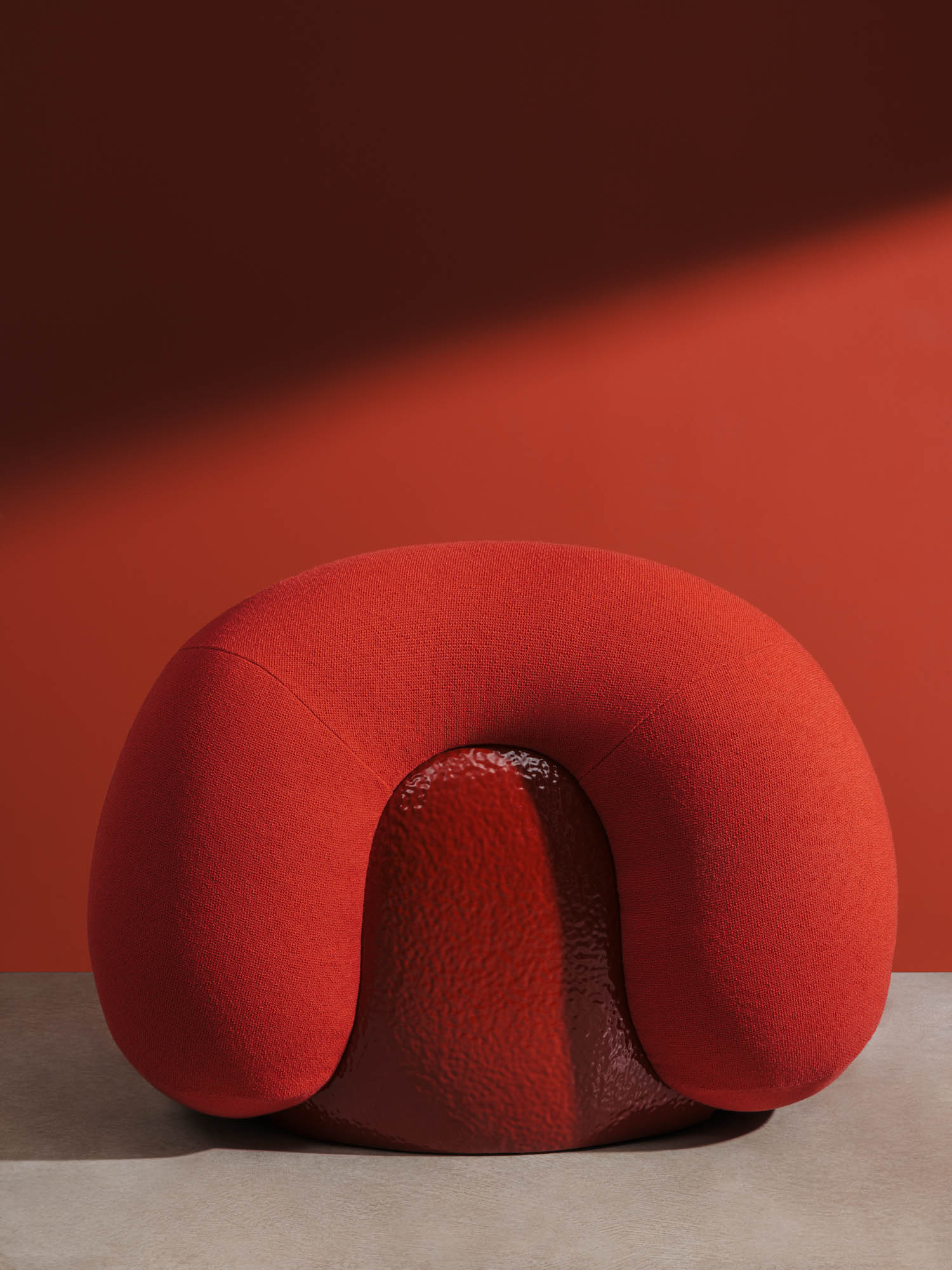 A modern, red armchair with a rounded, plush backrest and textured seat is placed against a solid red wall and neutral floor.