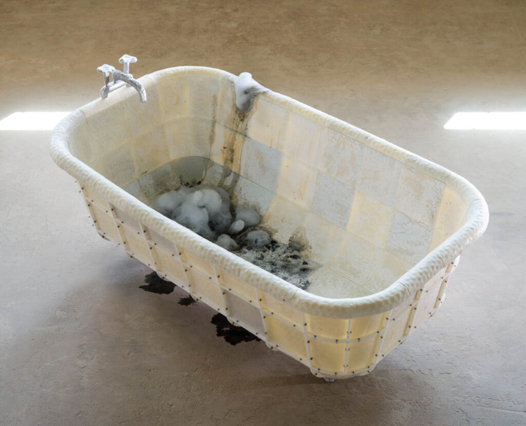 A tiled bathtub structure containing water and foam sits on a concrete floor.