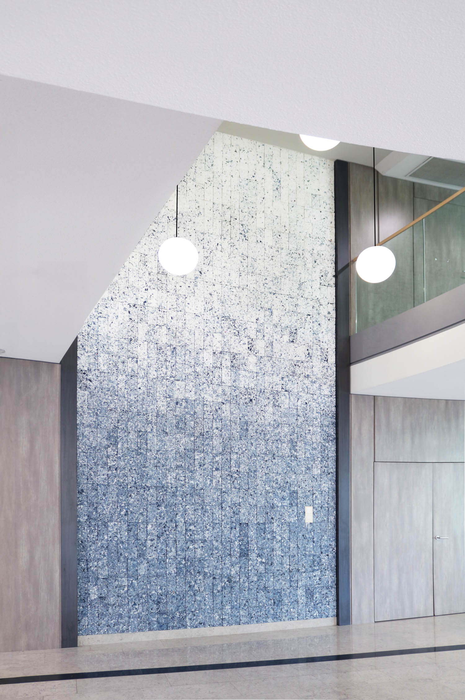 A tall accent wall with a blue and white speckled gradient pattern, flanked by wood-paneled walls and illuminated by two globe pendant lights.