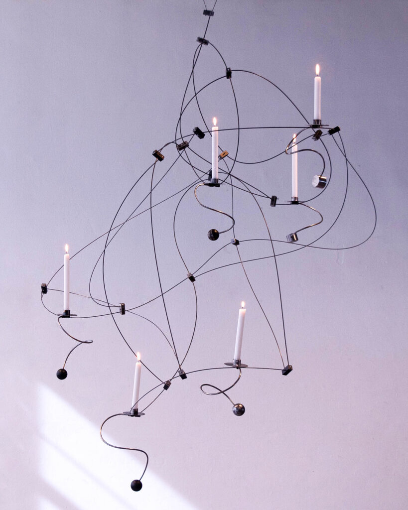 A suspended wire chandelier with six lit taper candles.