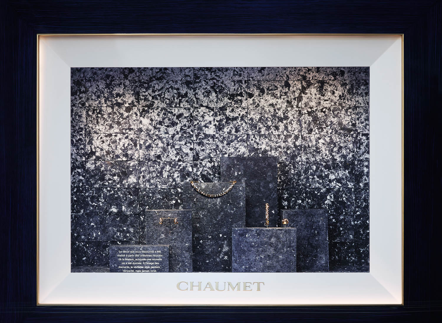 Chaumet jewelry display with a necklace, bracelet, and ring on stone pedestals in front of a patterned wall.