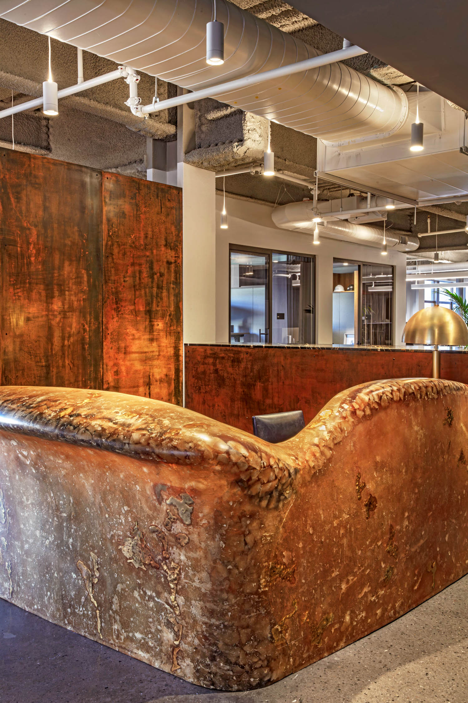 A curved, textured reception desk with a rustic, copper-like patina in an open-plan office.
