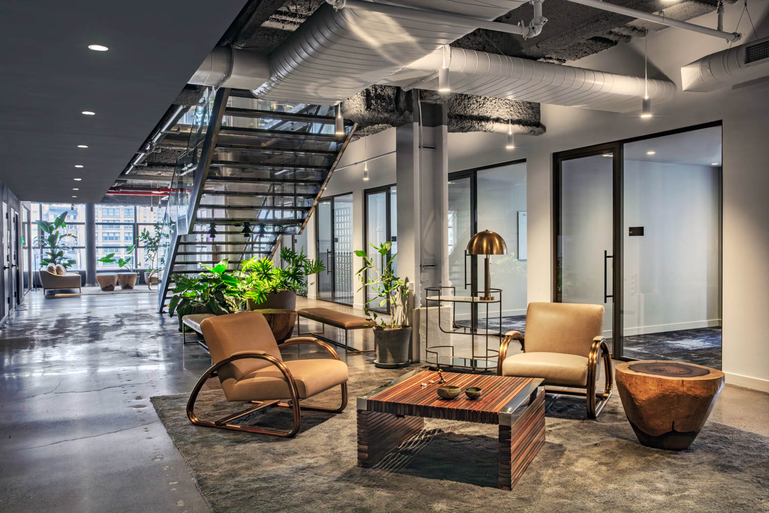 Modern office lobby with two lounge chairs, a slatted wooden coffee table, and a glass staircase.