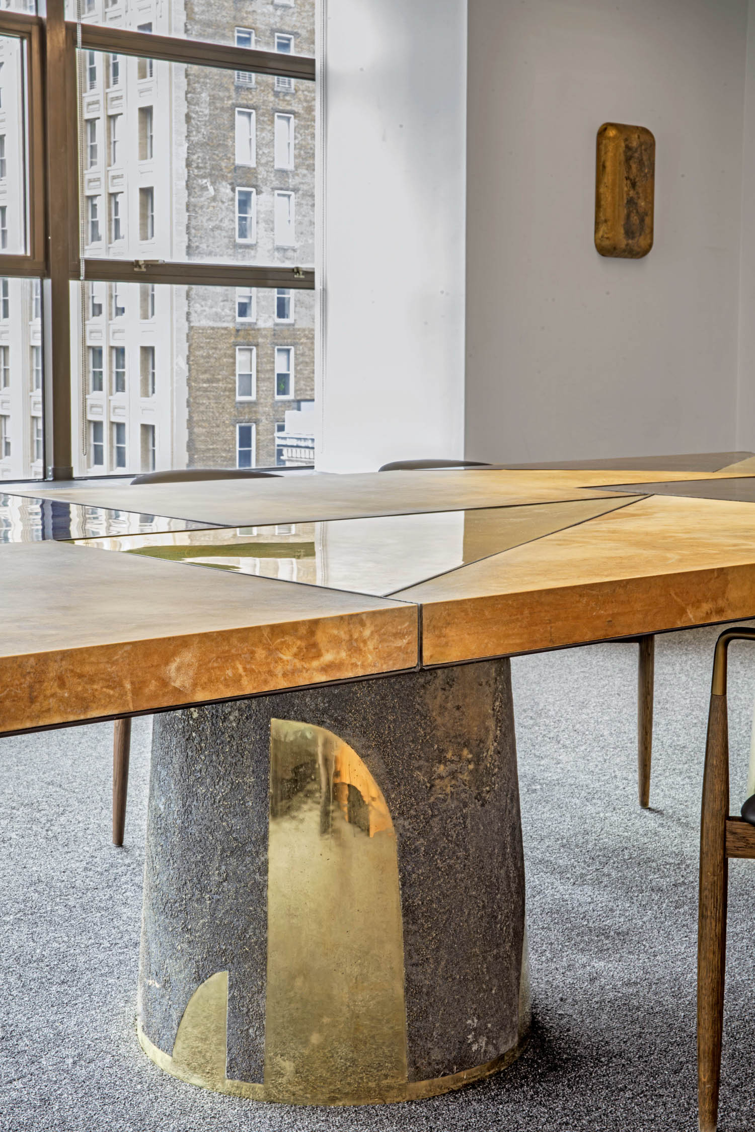 A conference table with a polished wood surface and a central glass inlay, supported by a cylindrical concrete base with brass accents.