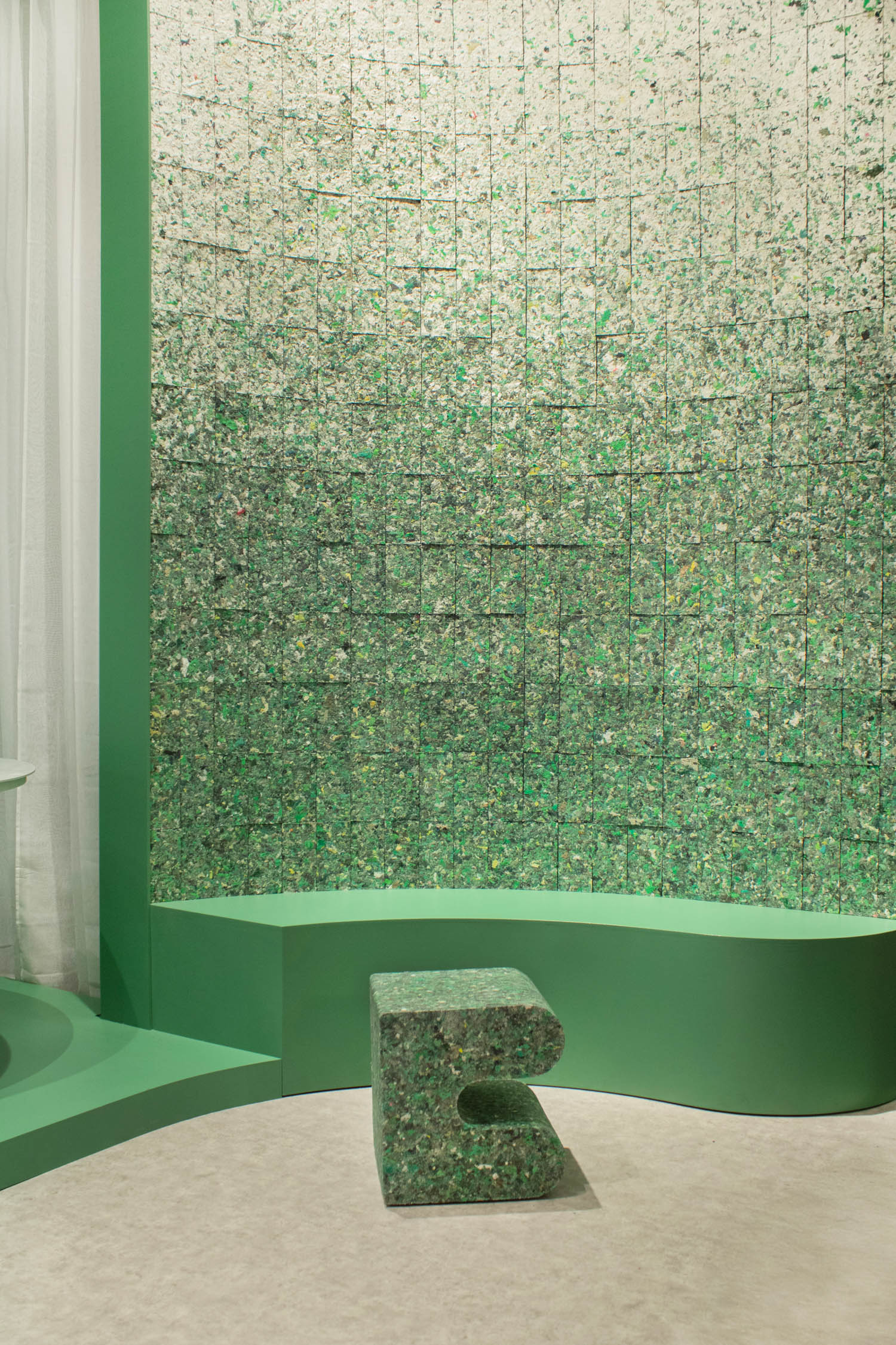 A curved wall covered in green speckled tiles, with a matching low bench and a U-shaped stool in front.