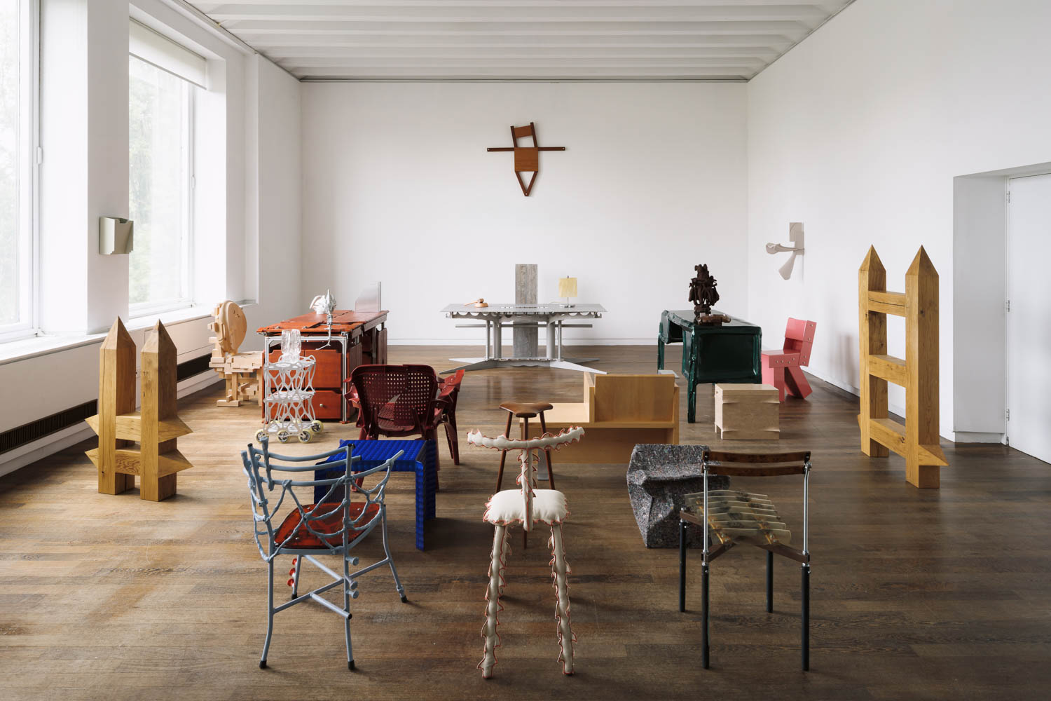 An art gallery display featuring various sculptural chairs, tables, and wooden objects arranged across a wood floor.