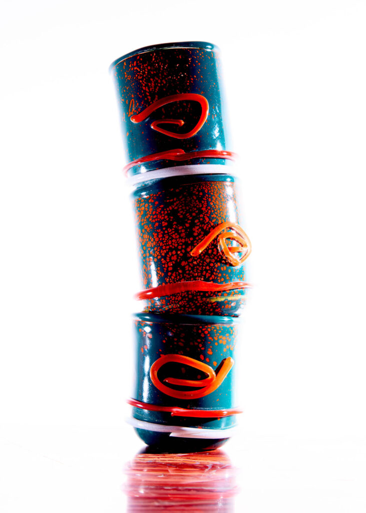 A vertical stack of three cylindrical glass vessels, each dark blue with orange flecks and a decorative orange swirl.