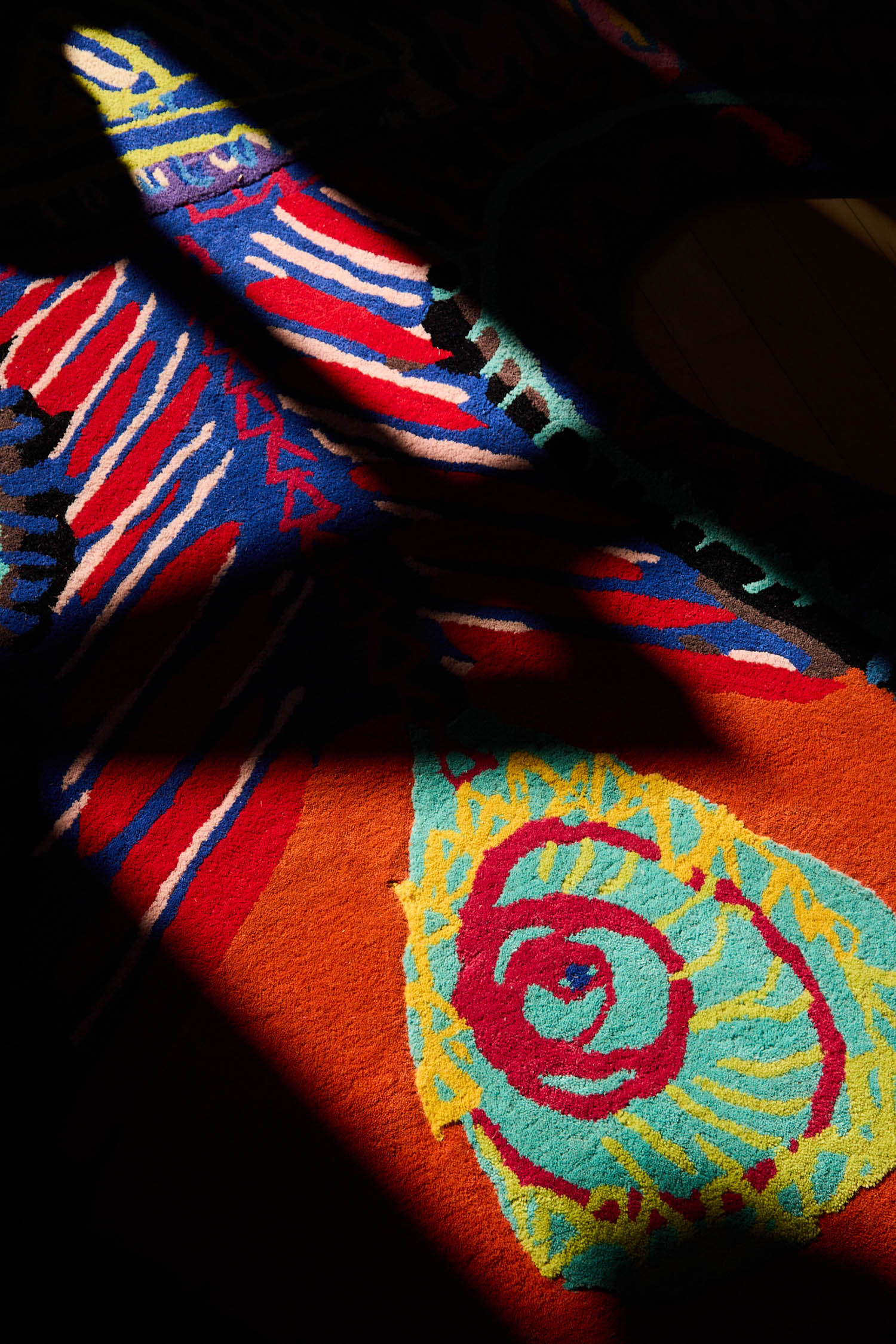 A rug with a vibrant, abstract, multicolored pattern folded to cast a prominent shadow.