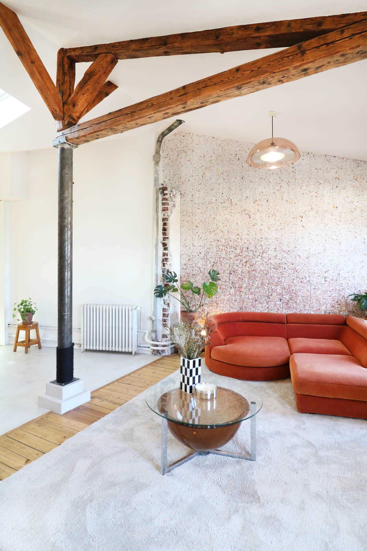 A living room with an orange sectional sofa, a glass-topped coffee table, and exposed wooden ceiling beams.
