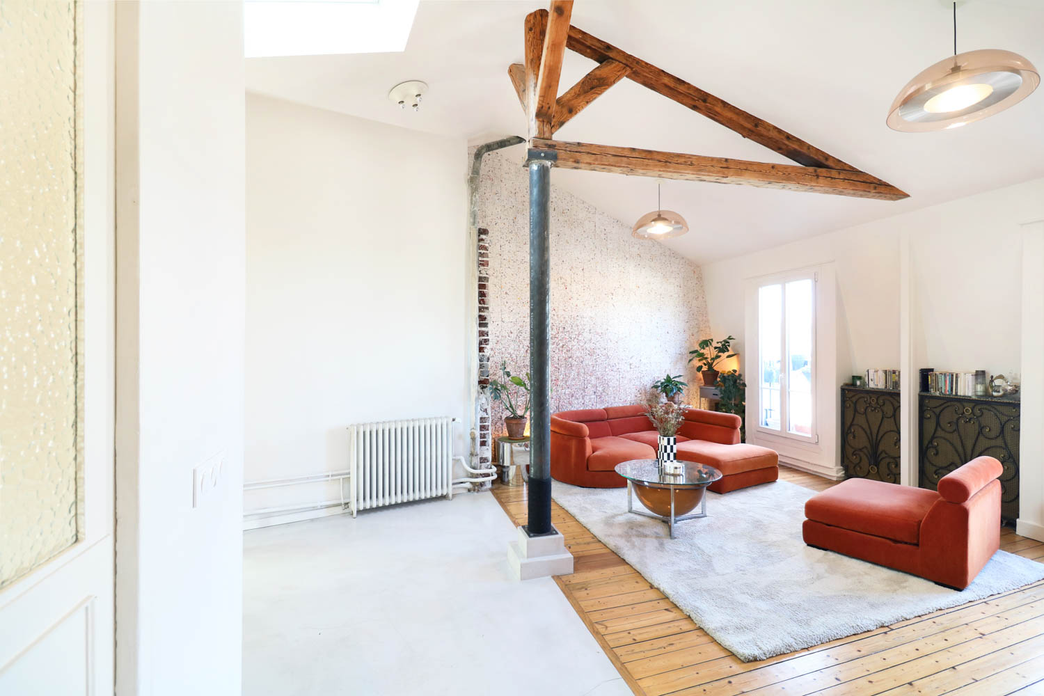 Living room with orange modular sofas, a round glass coffee table, and a central metal support beam under a wooden vaulted ceiling.