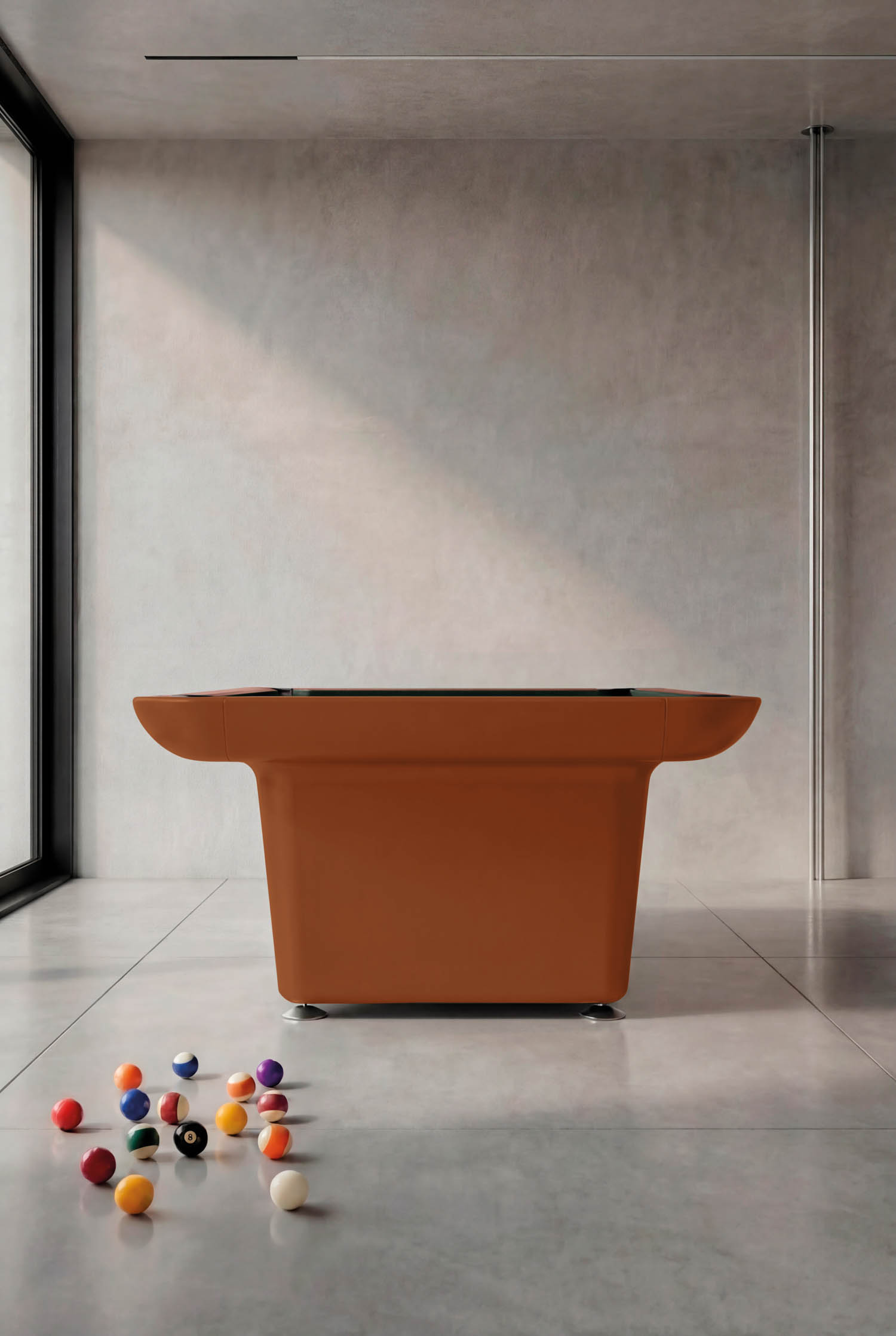A modern brown pool table sits in a minimalist room with scattered billiard balls on the floor and large windows letting in natural light.
